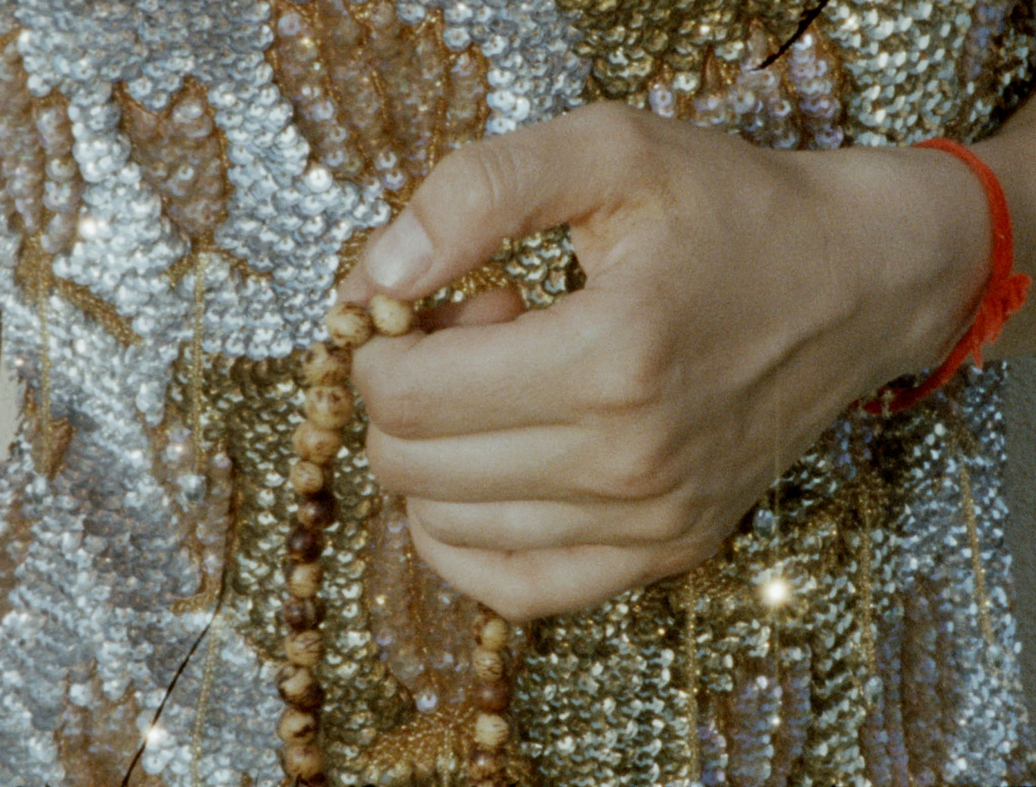 16mm film still: a closeup of a hand telling the beads of a rosary