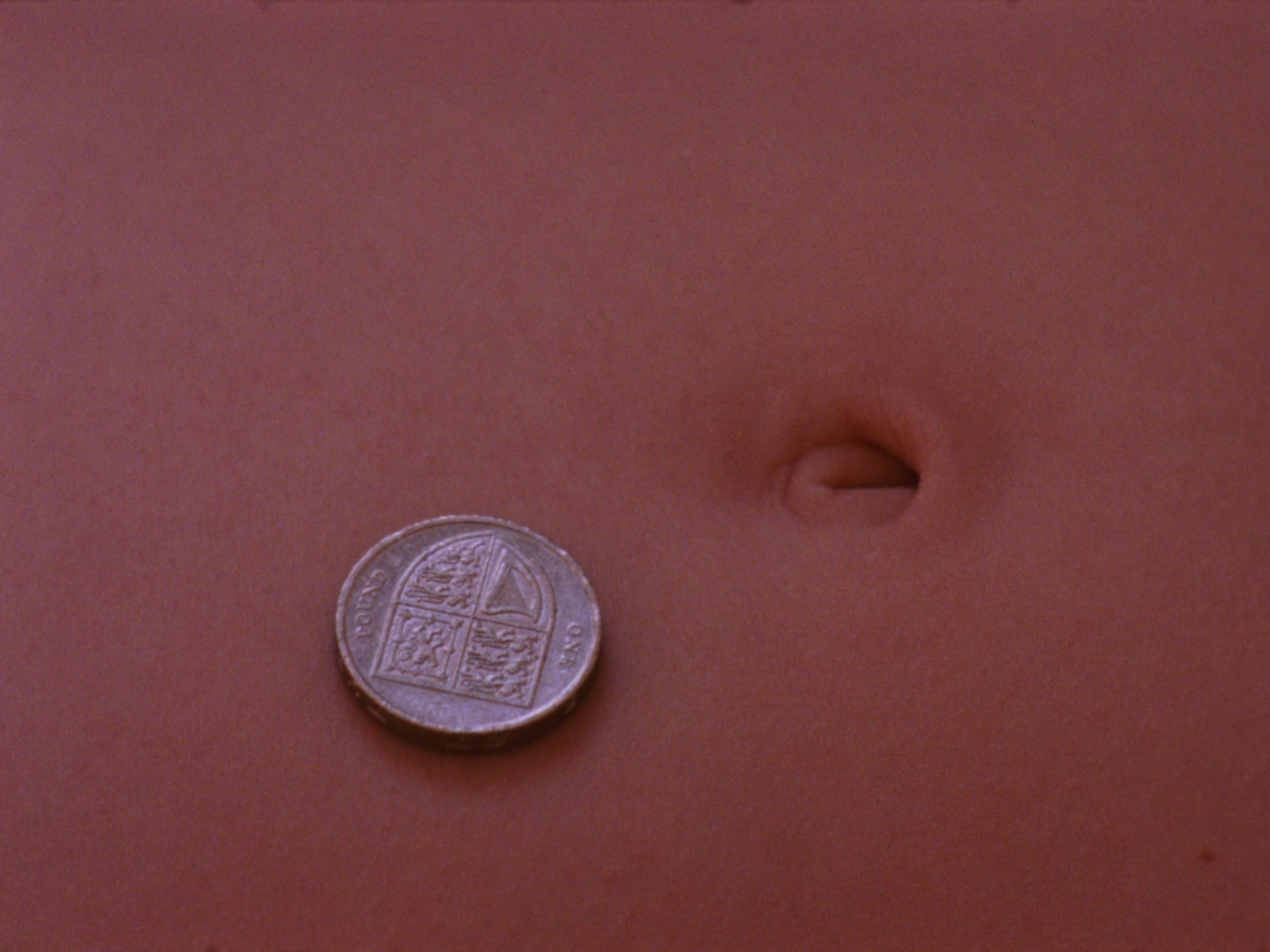16mm film still: a one pond coin next to someone's bellybutton