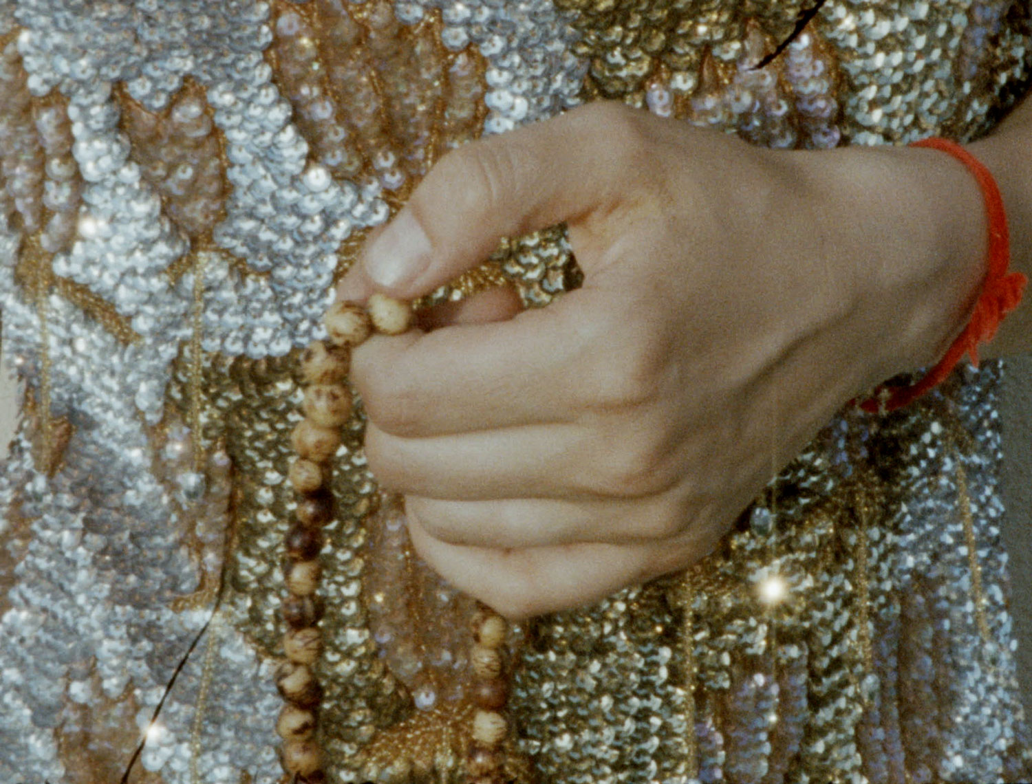 16mm film still: a closeup of a hand telling the beads of a rosary