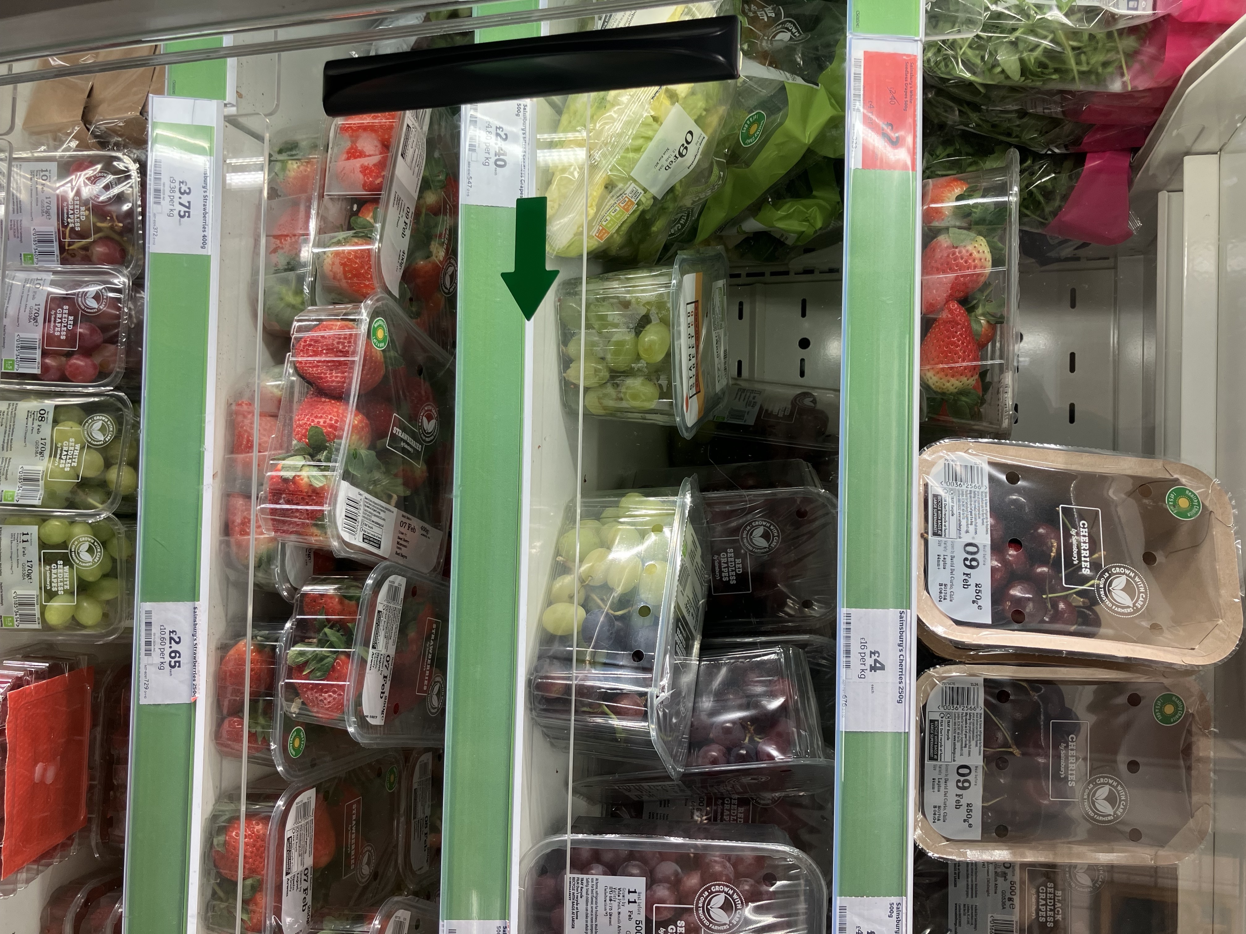 A phone photo of fruits and greens in a supermarket refrigerated display, tilted 90 degrees