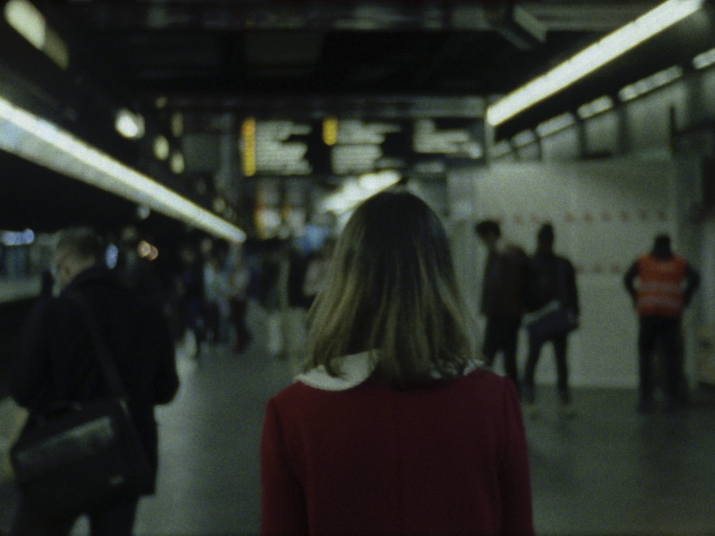 16mm film still: a woman in a red dress walking in a station of the rapid transit system in Paris