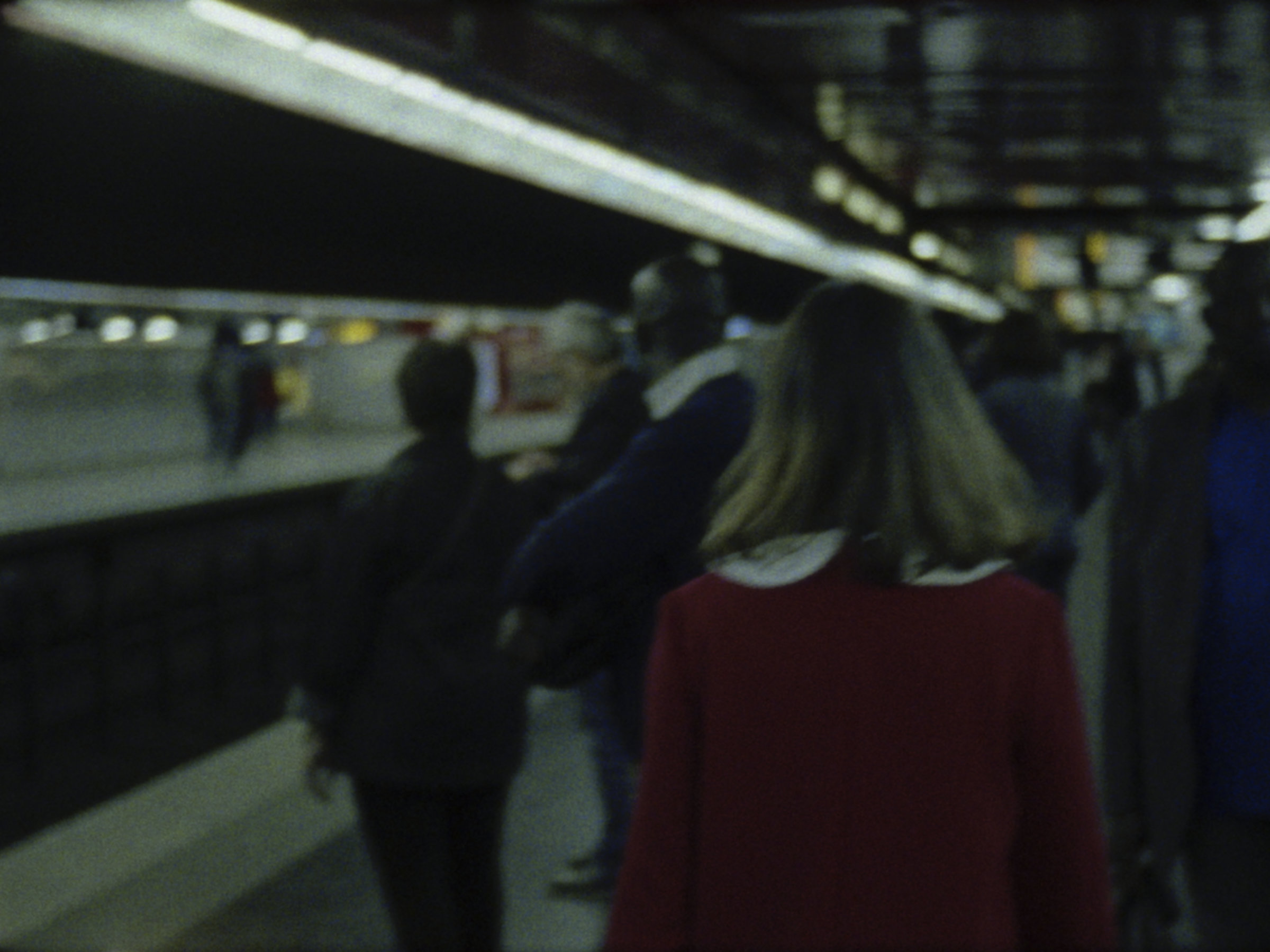 16mm film still: a woman in a red dress walking in a station of the rapid transit system in Paris