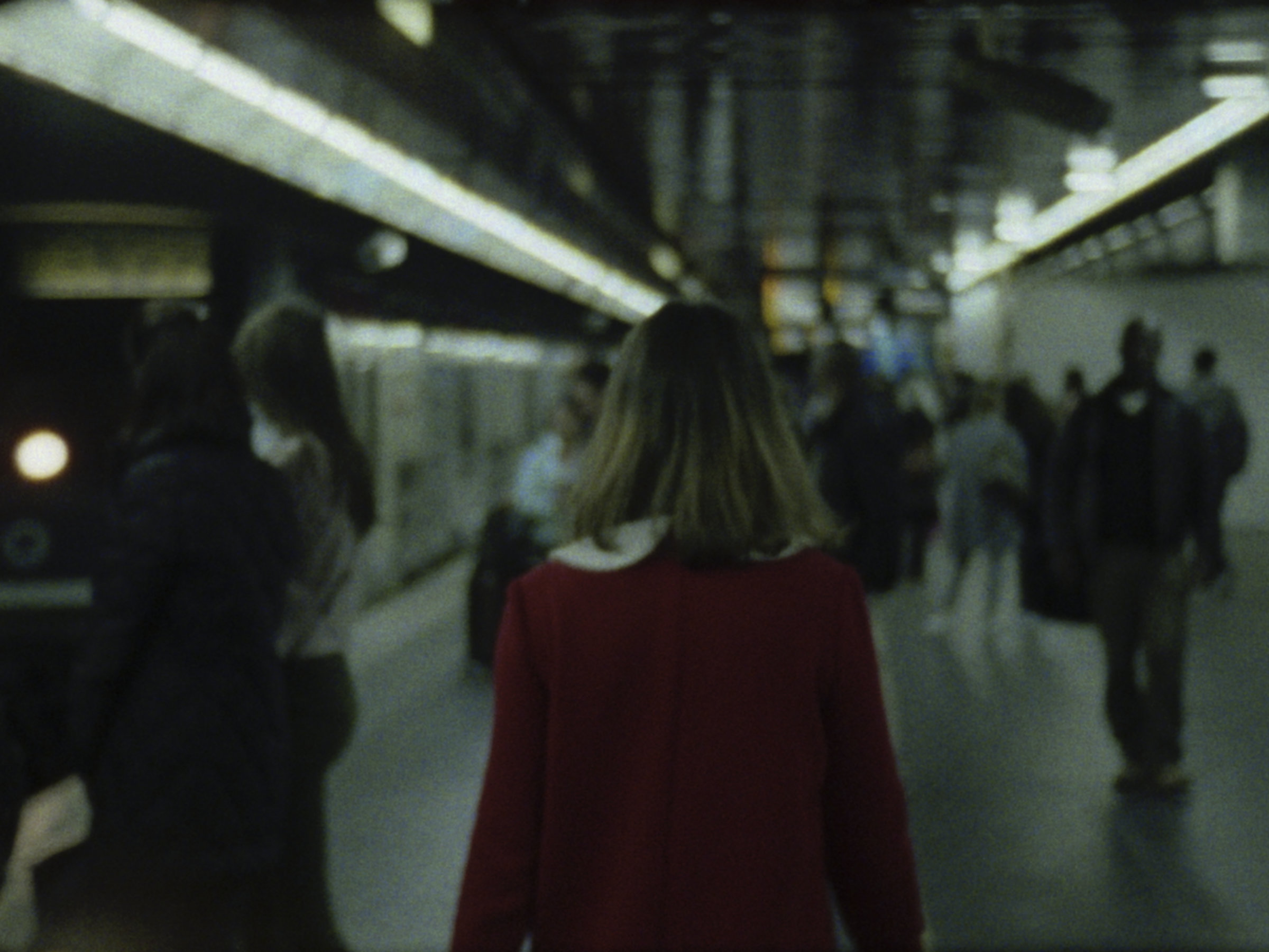 16mm film still: a woman in a red dress walking in a station of the rapid transit system in Paris