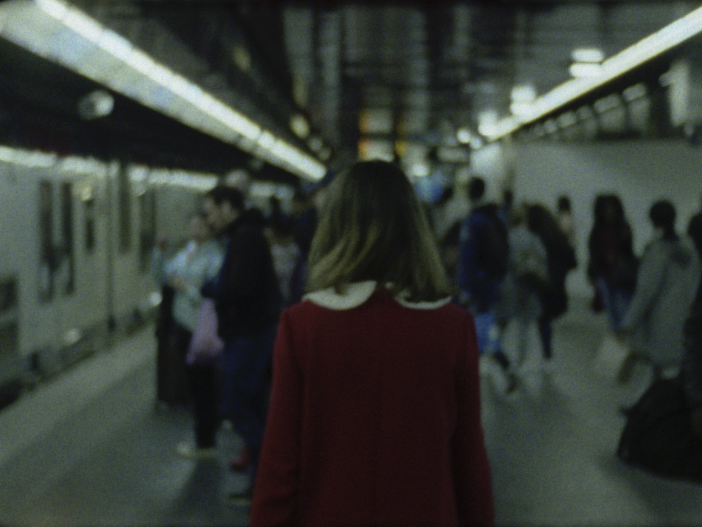 16mm film still: a woman in a red dress walking in a station of the rapid transit system in Paris