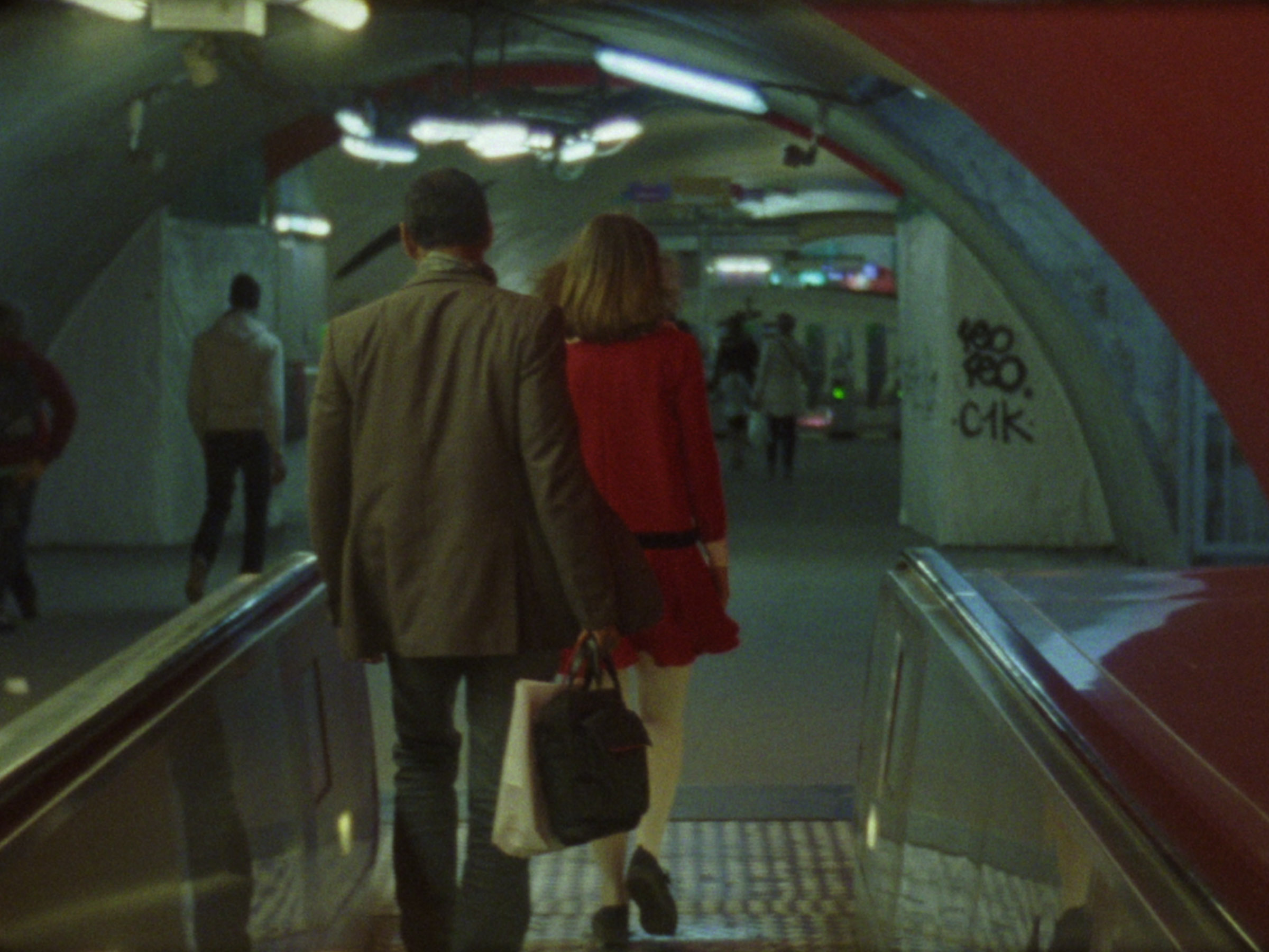 16mm film still: a woman in a red dress walking in a station of the rapid transit system in Paris