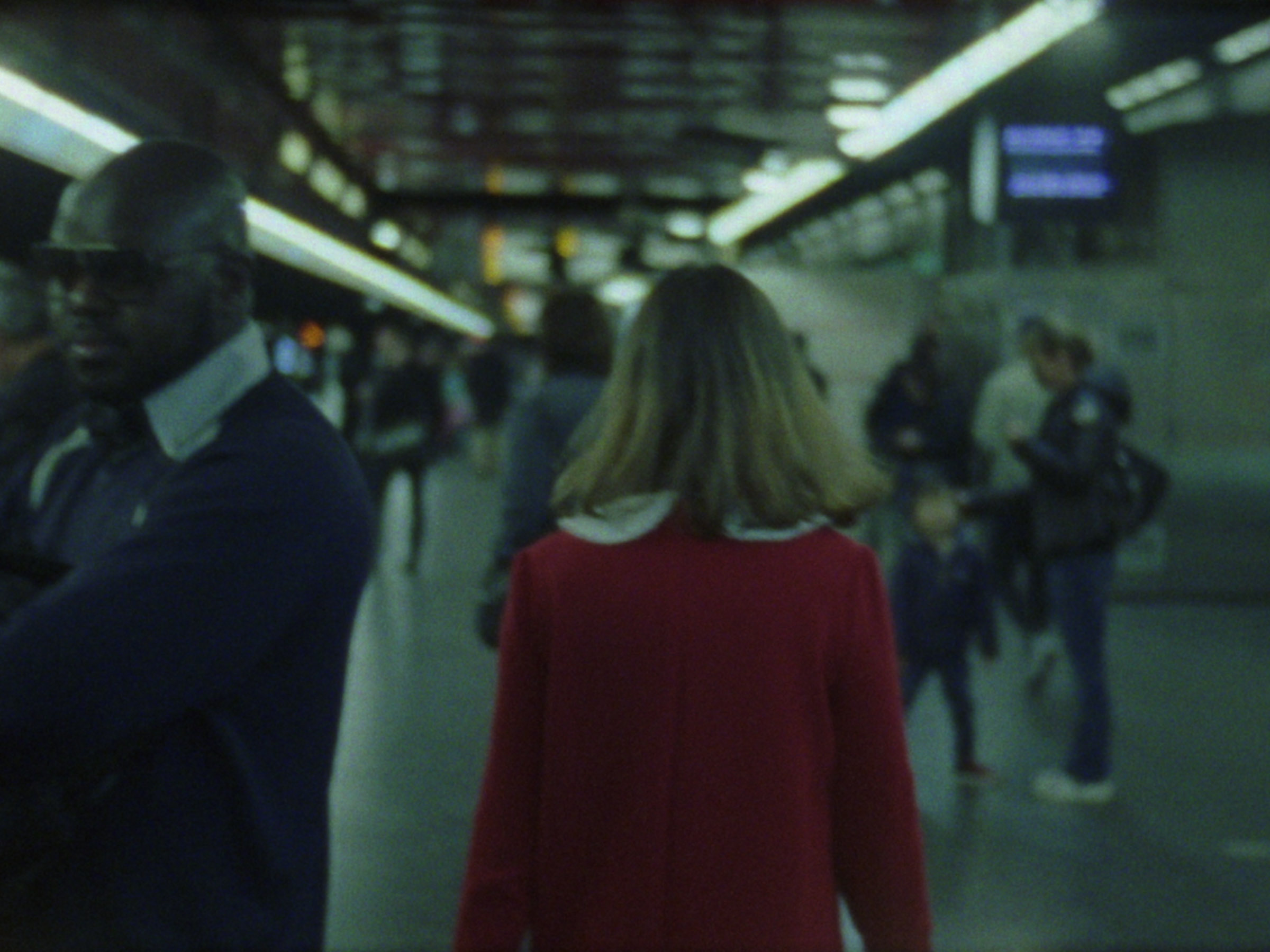 16mm film still: a woman in a red dress walking in a station of the rapid transit system in Paris